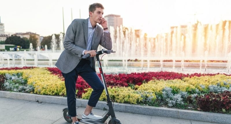 man in suit on e scooter speaking on phone